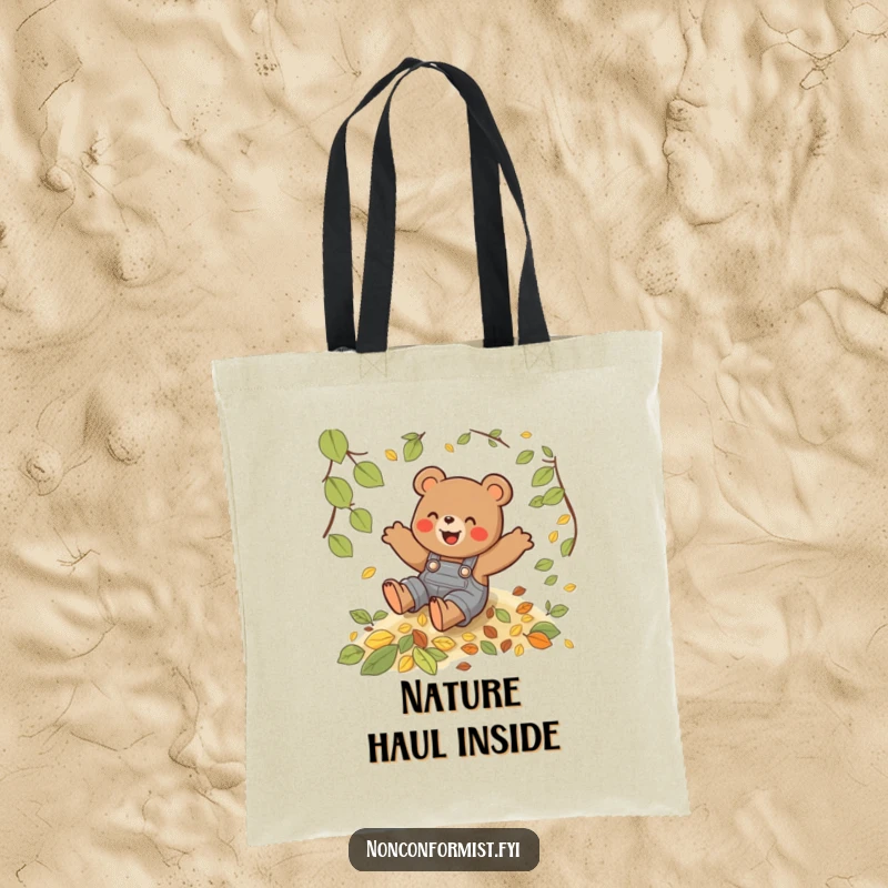 Funny tote bag depicting a playful bear in overalls joyfully sliding down a hill of colorful autumn leaves.